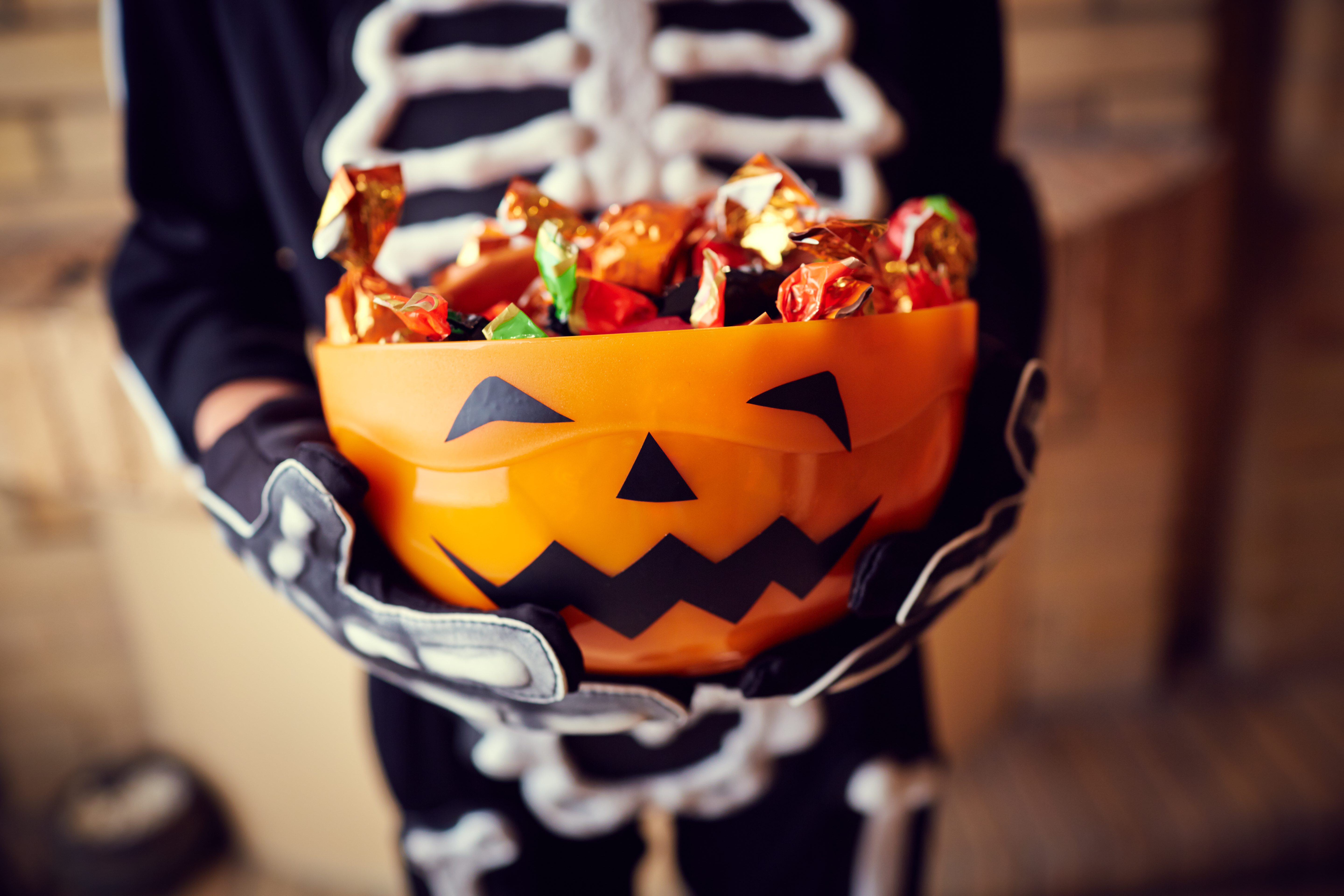 Halloween candy in a bowl held by a child dressed as a skeleton.