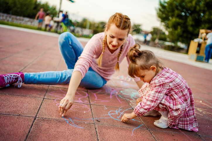 A mother and daughter draw with chalk at a playground.