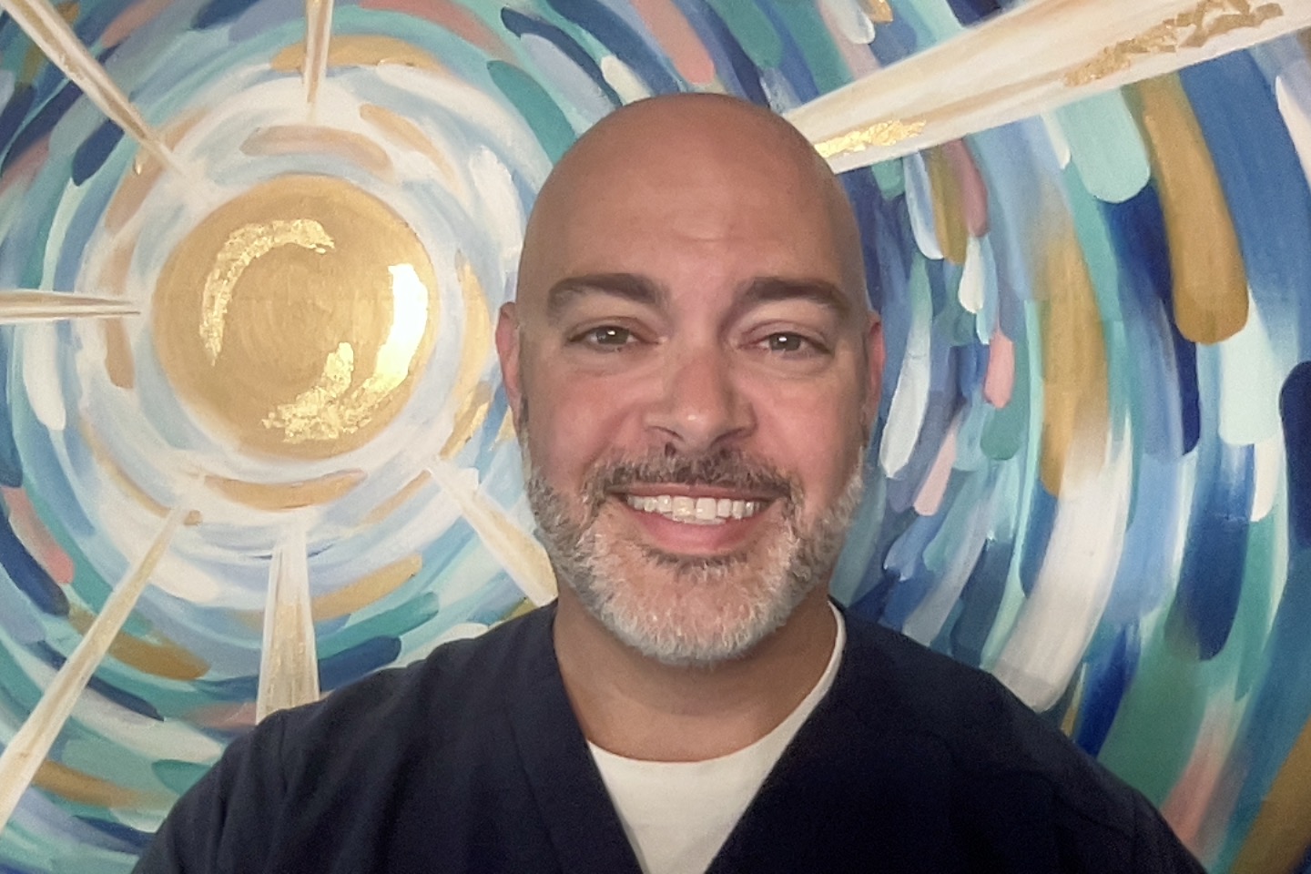 Aaron Harris, APRN, stands in front of a painting of the sun