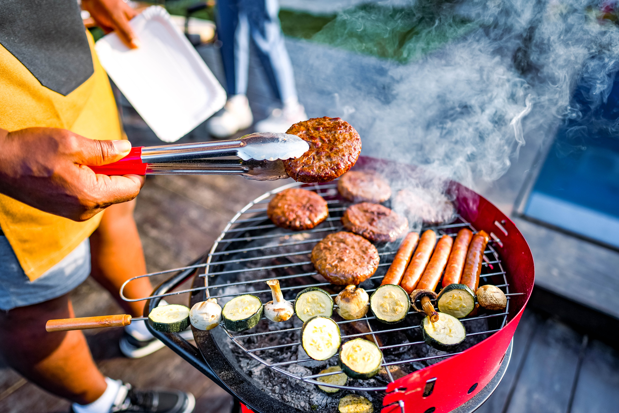 Burgers, hot dogs and vegetables on a charcoal grill.
