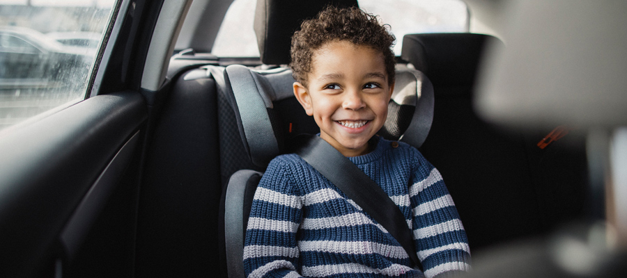 A young boy smiles while sitting in the backseat of a car. 