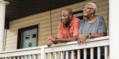 A couple stands side by side on a porch. 