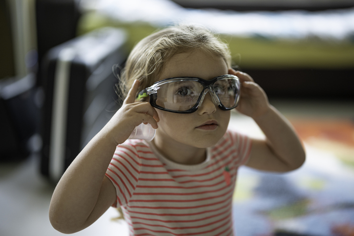 A small child wears protective goggles, holding them to their face