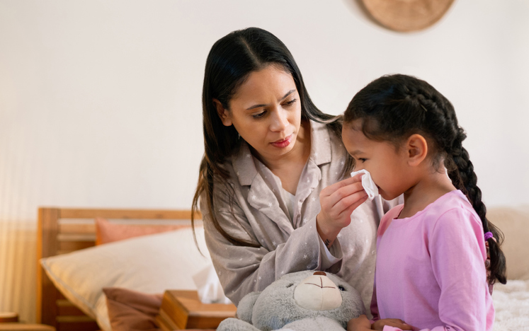 Women helping young girl blow her nose. 