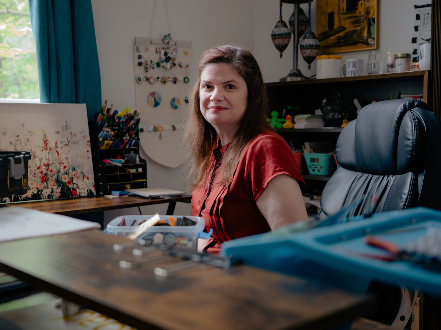 Nicola Allen seated at a sewing table. She's wearing a red shirt and smiling toward the camera.