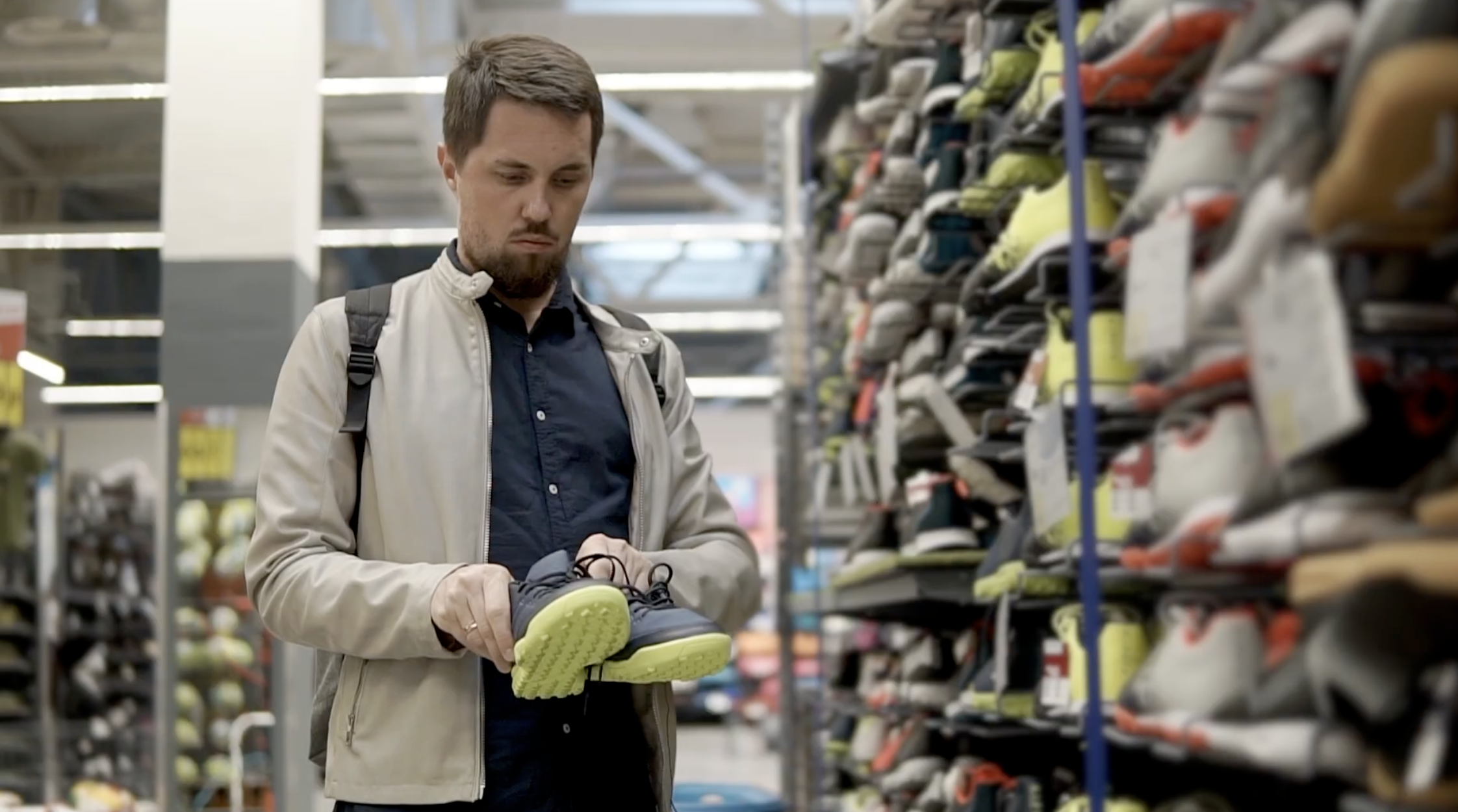 A man looks curiously at a pair of shoes. He is in a shoe store.