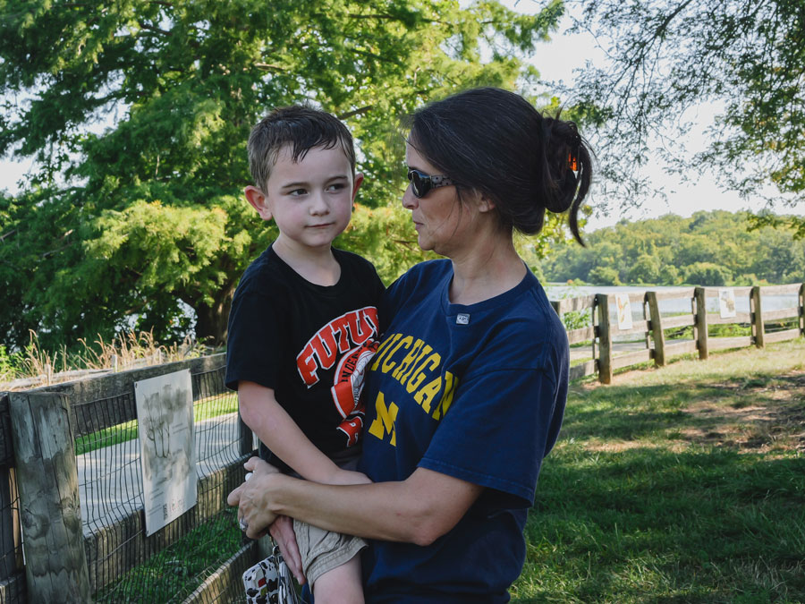 Granger Smith is held by his mother while the two stand near a fence at a park. Granger has a mischievous look on his face.
