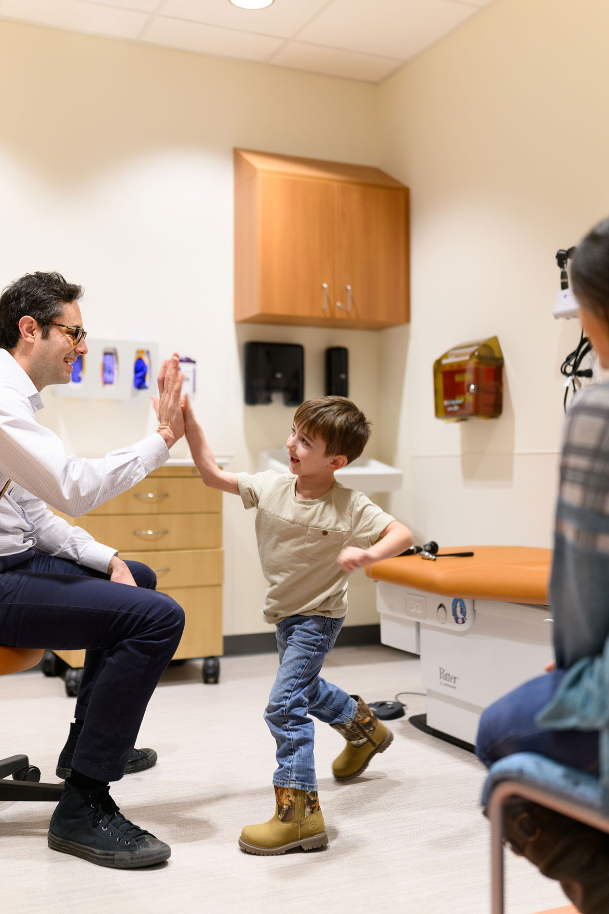 Granger Smith, center, gives a high five to Dr. David Neil Toupin, left, who's seated in a rolling chair. Granger's mother is slightly visible to the right.