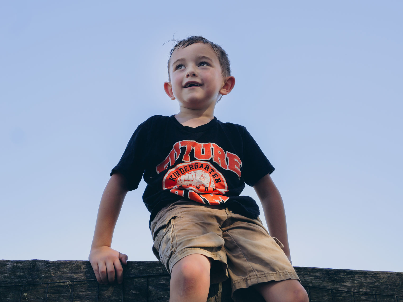 A young kid, Granger Smith, sits on a fence railing and looks toward the sky. He's wearing a black shirt that says "Future"