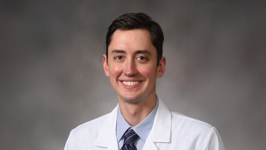 Dr. Peter Haigh posed against a gray background, smiling