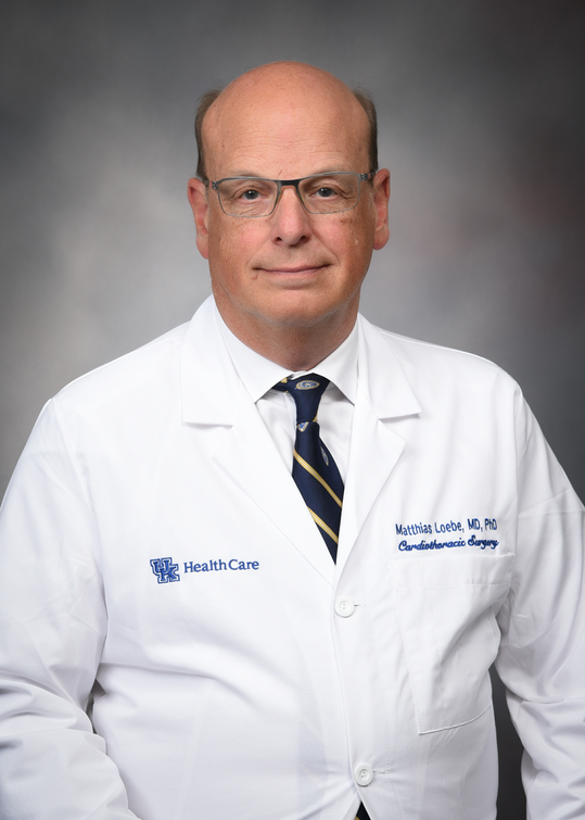 Dr. Matthias Loebe poses against a gray background wearing a white medical coat with her name written on it.
