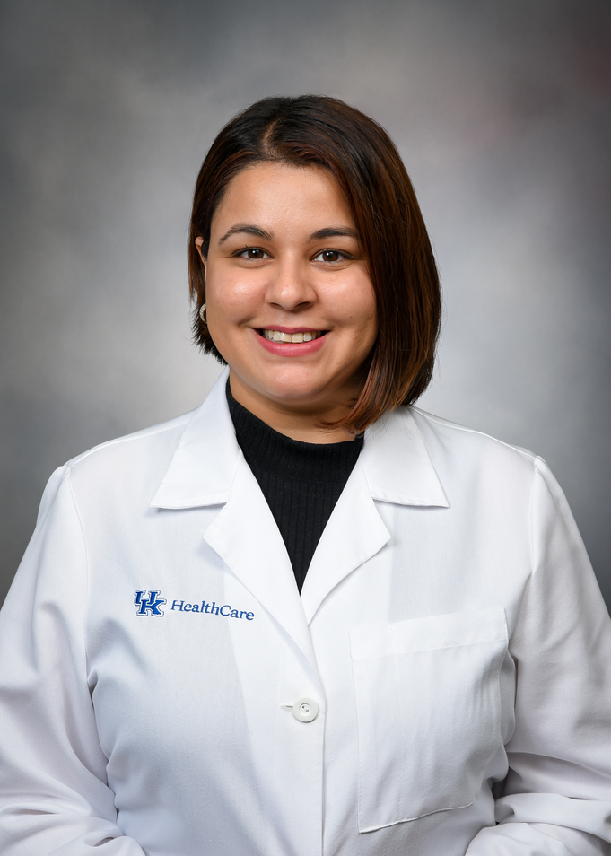 Dr. Naureen Narula poses against a gray background wearing a white medical coat.