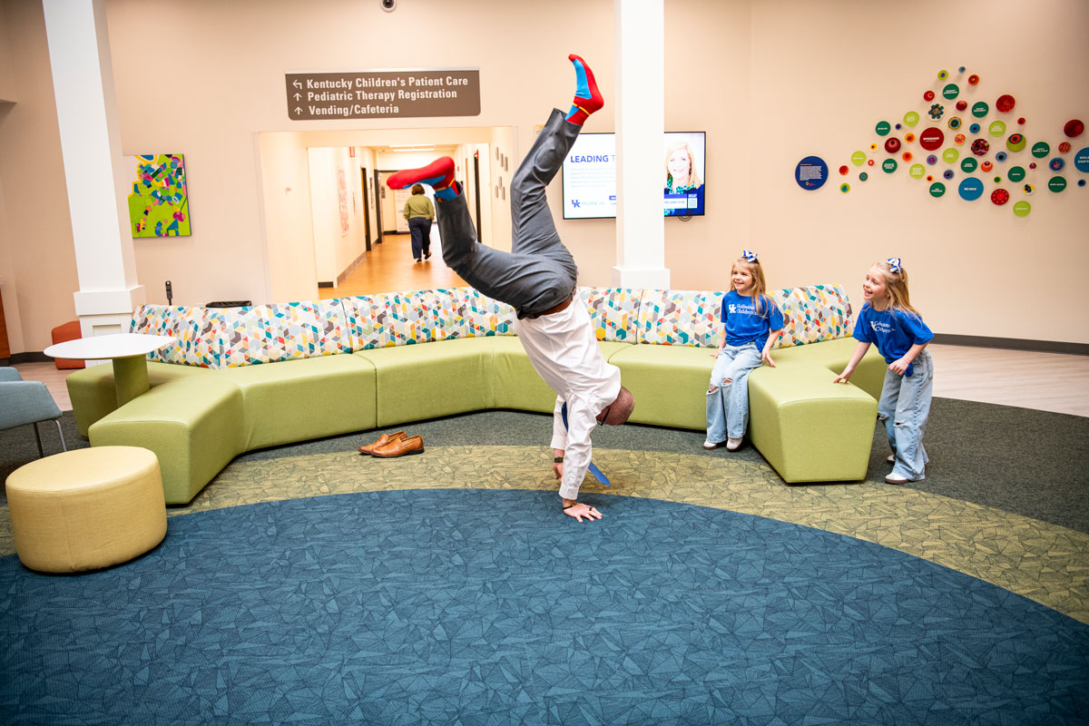 Dr. Scottie Day standing on his hands in a lobby area as two kids watch in delight