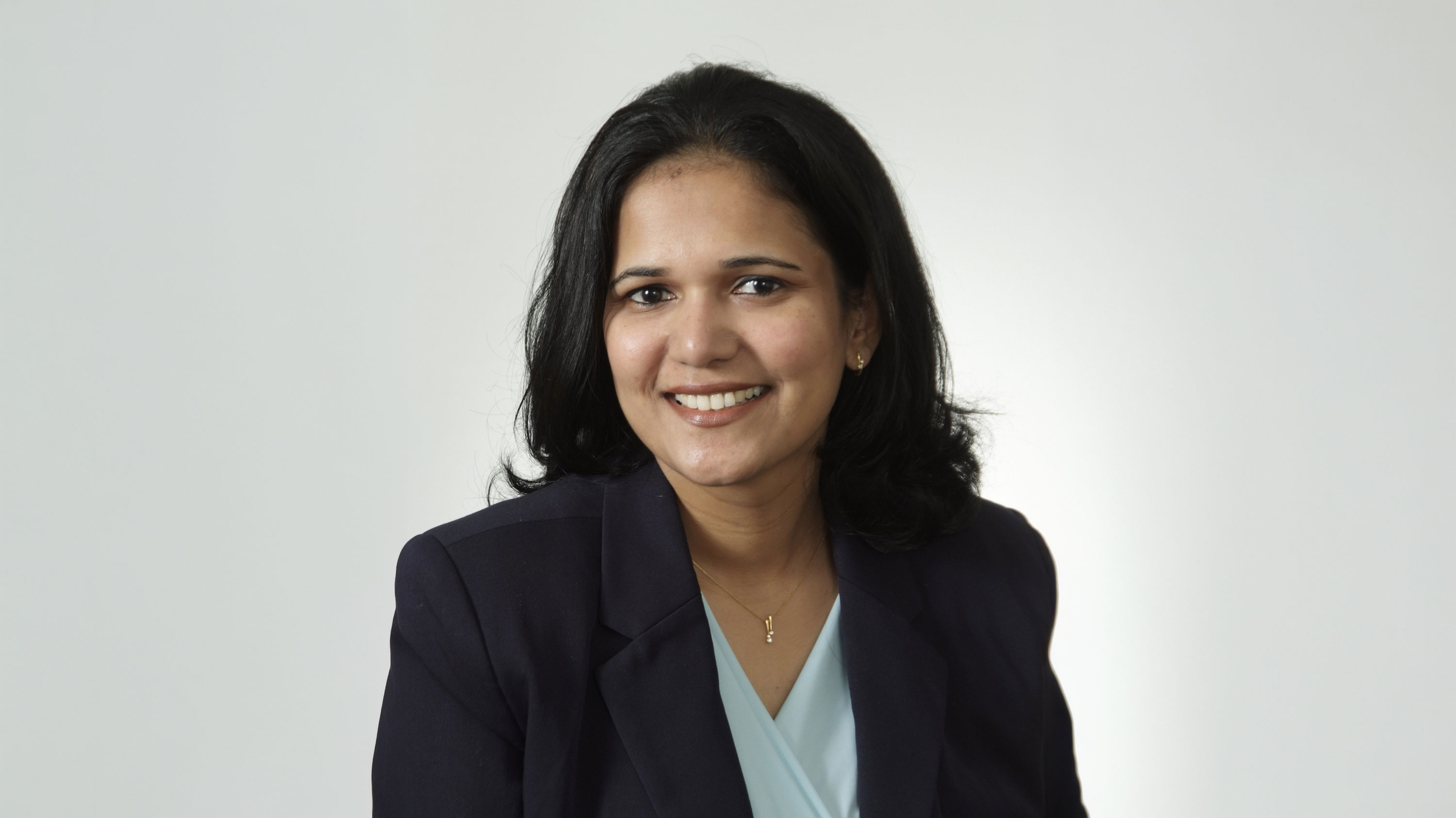 Dr. Sally Mathias, wearing a black blazer against a white backdrop, looking toward camera