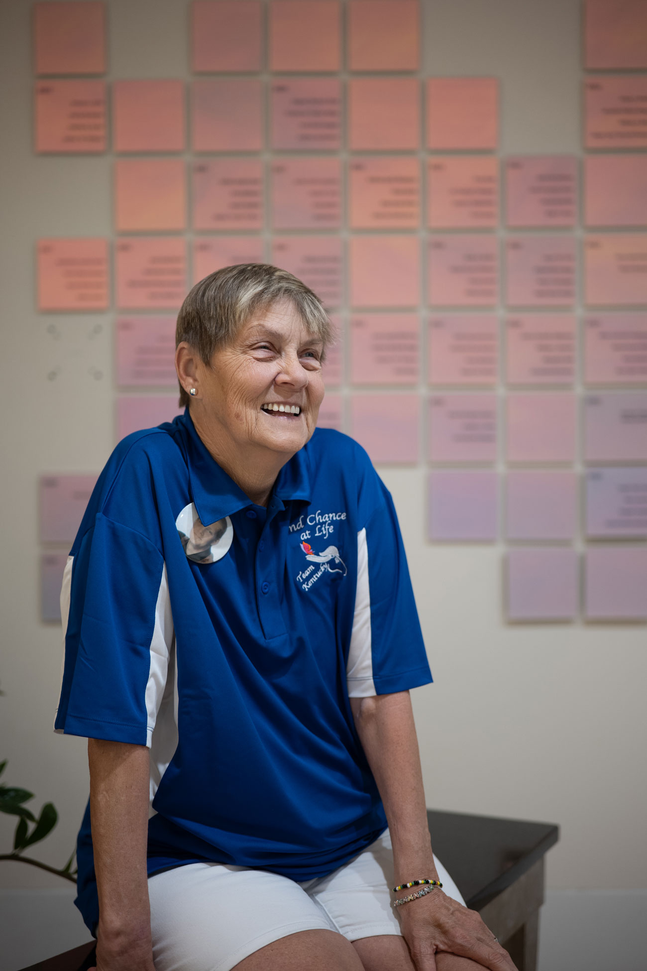 Sallie Wilson smiling to someone off camera against a donor wall located at UK HealthCare