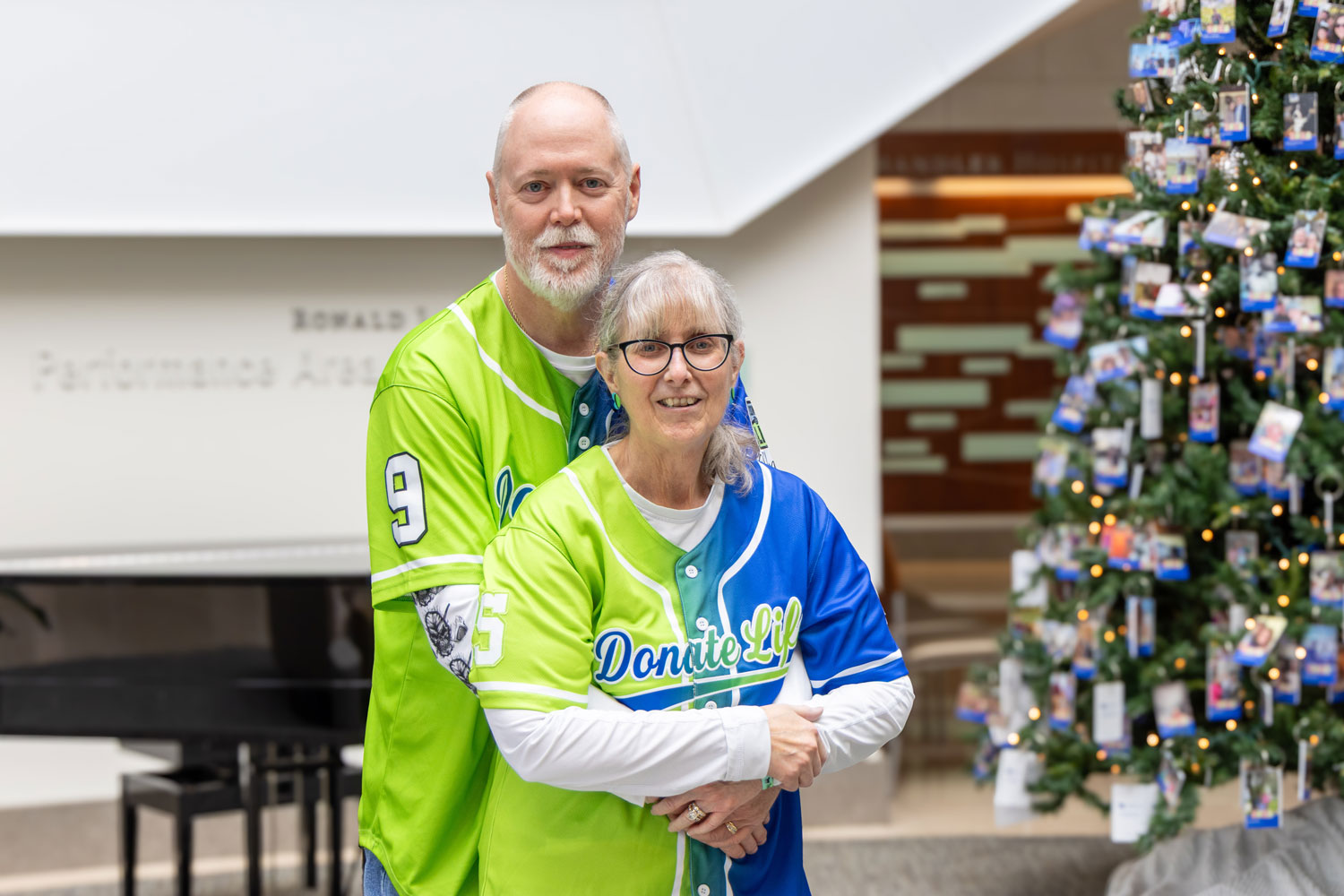 Tom and Debbie Coleman poses for a portrait in the lobby of UK Albert B. Chandler Hospital. They're hugging and wearing special jerseys showing their support for organ transplant 