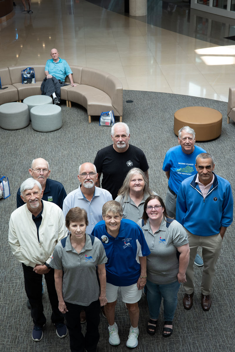 A group of 10 transplant patients gathered in the lobby of UK Albert B. Chandler Hospital for a photo op. A man is on the couch in the background.