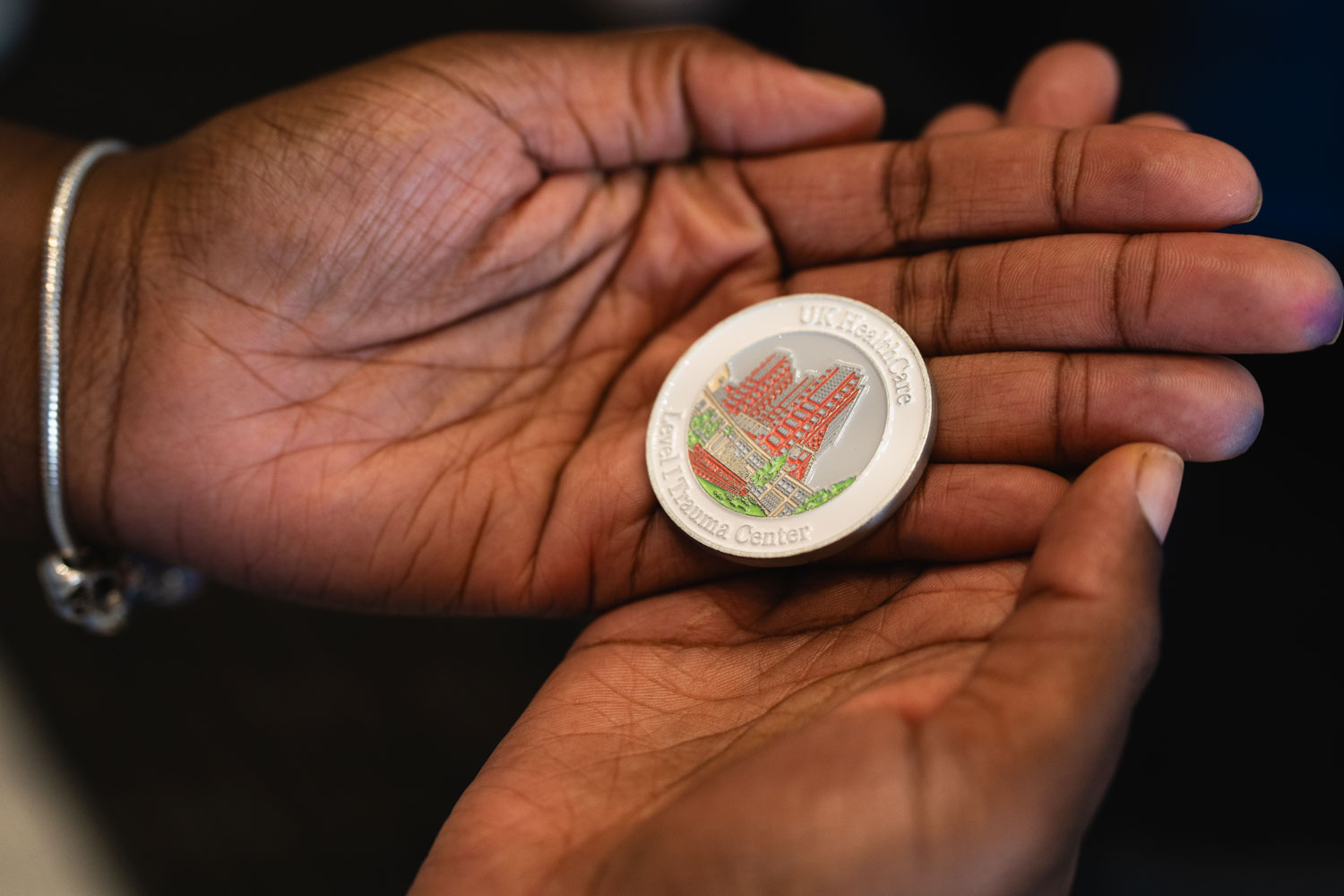 A middle close-up shot of a challenge coin inscribed with an image of UK Albert B. Chandler Hospital and words indicating it is a Level I Trauma Center, held in an unknown person's hands