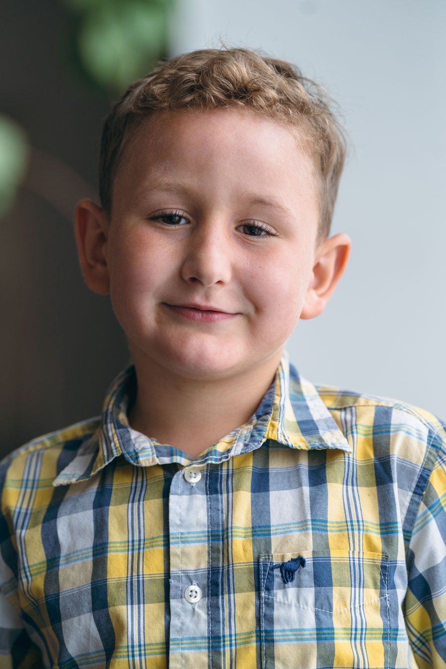Child Oliver Blair, wearing a flannel-colored shirt, smiles at camera