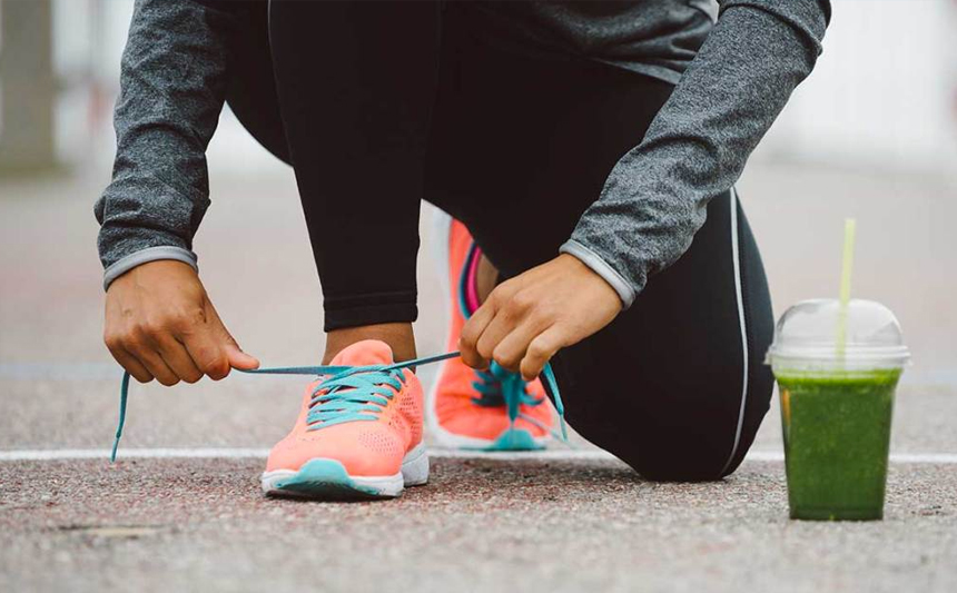 Runner rests smoothie on the pavement while tying shoelace.