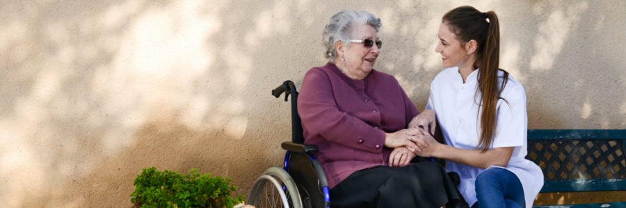 A caregiver talks with an elderly female patient in a wheelchair.