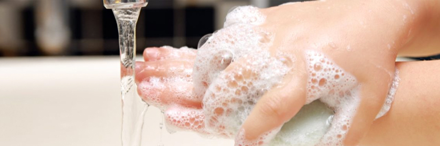 A child's hands covered in soap bubbles under running water.