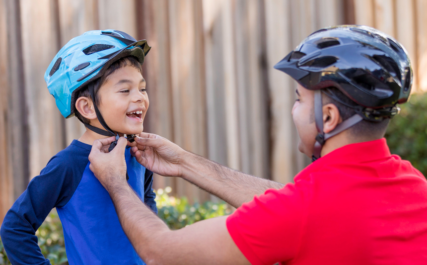 A father adjusts his son's bicycle helmet.