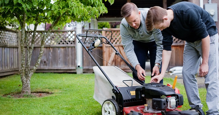 A father teaches his son about a lawn mower.