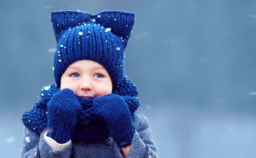 A child in mittens and knit hat outside in the snow.