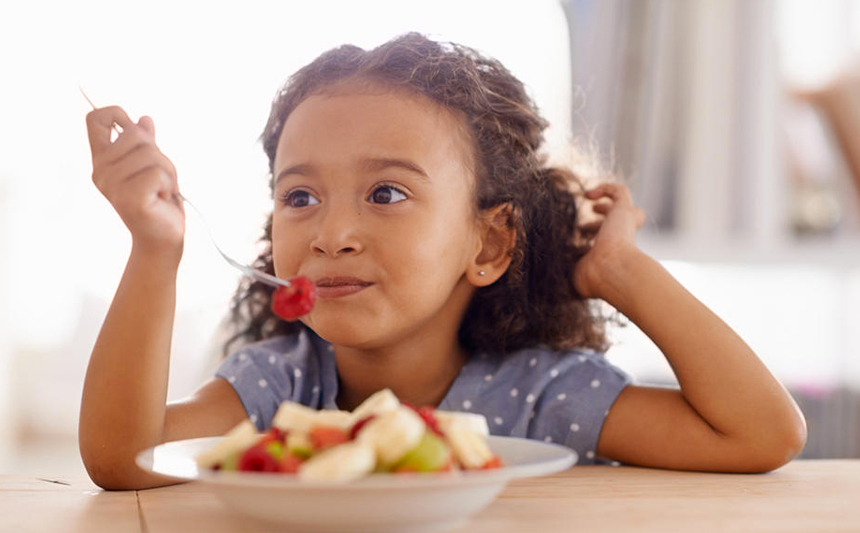 A little girl eats a bowl of fruit.