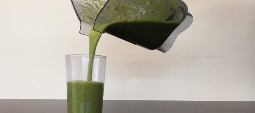 A person pours a green smoothie into a glass
