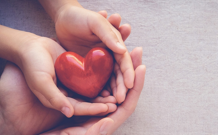 Adult and child's hands cradling a heart.