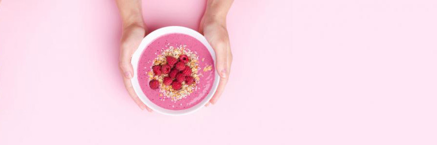 Holding bowl of yogurt and granola against a pink background.