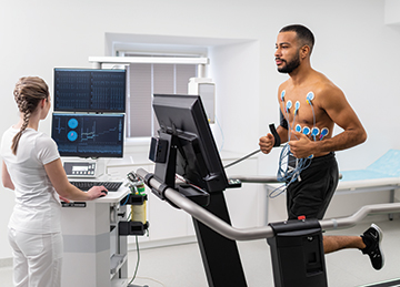 A man runs on a treadmill while a technician views his test results on a computer monitor. 