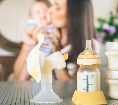 A breast milk pump and bottle with mother and baby in the background.