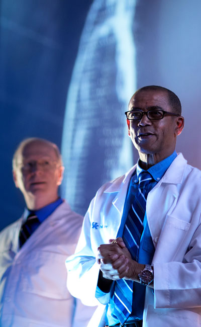 Two doctors giving a presentation before a large screen.