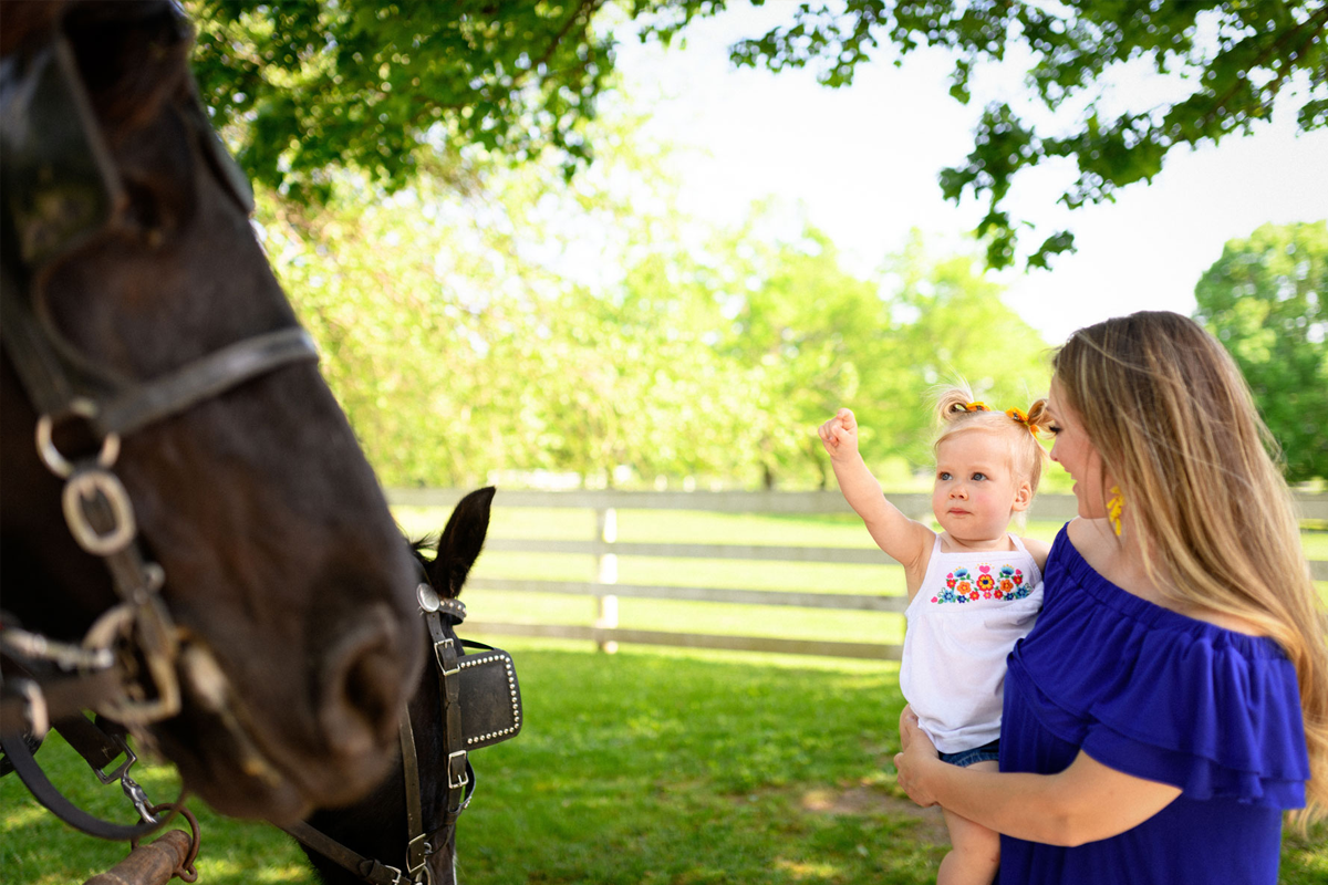 Courtney Watts holds her daughter, Jade, as they look at a horse.