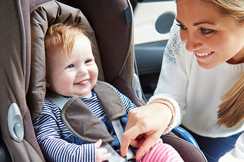 A mother adjusts her smiling toddler's carseat.