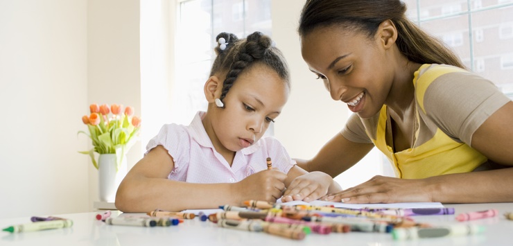 A mom helps her young daughter color.