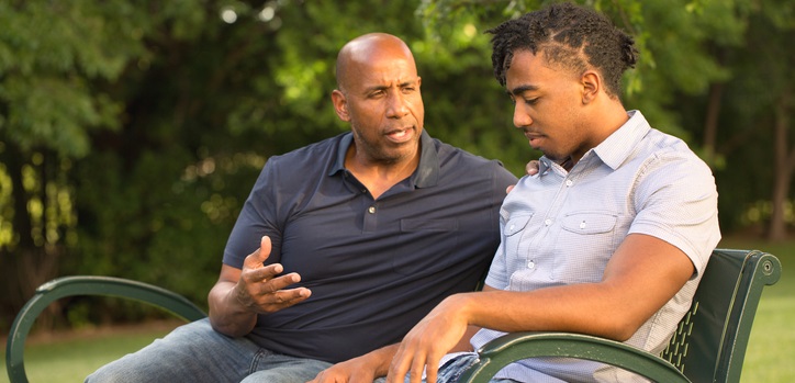 Father talks to his son on a park bench.