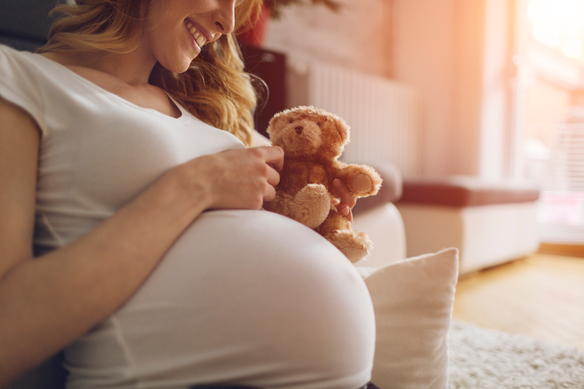 A pregnant woman holds a teddy bear.
