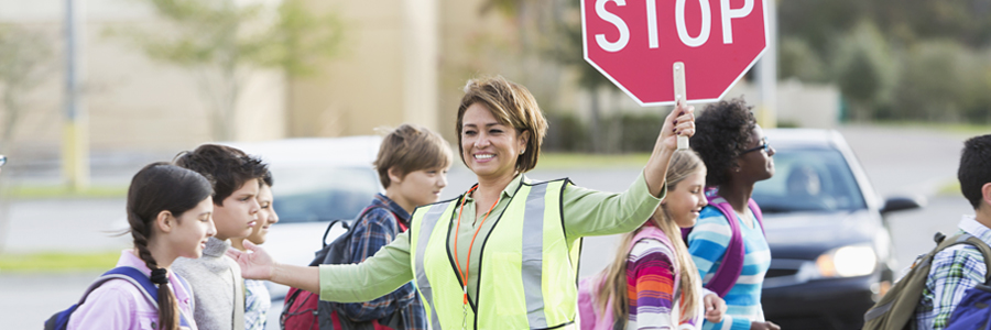 Middle school students cross the street with the assistance of a crossing guard with stop sign.