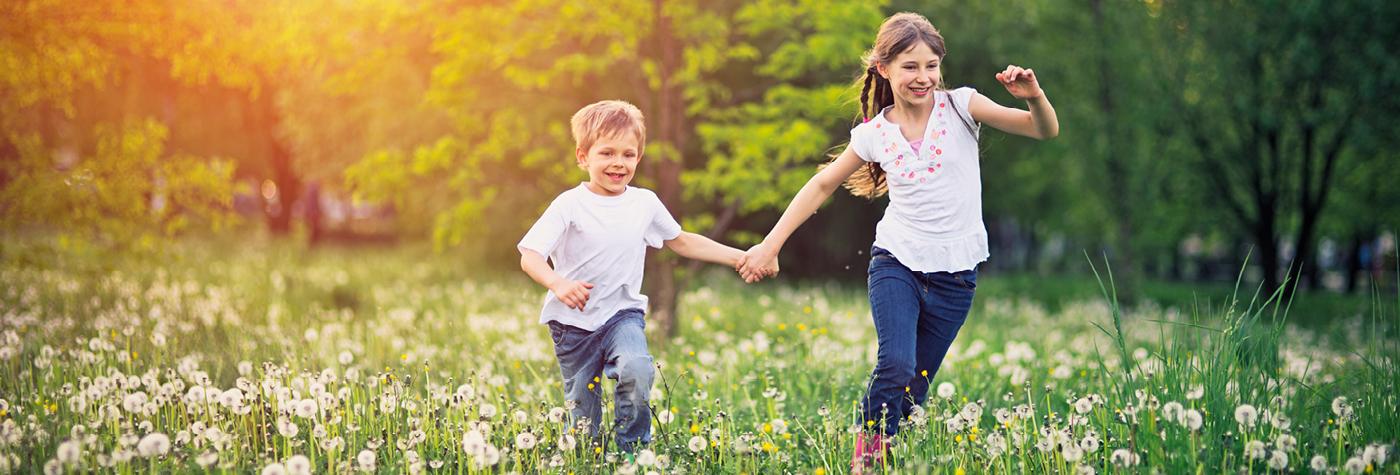 A young boy and girl hold hands as they run through a field of wildflowers together. 