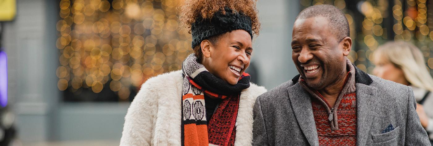 An African American couple walks together and laughs while wearing cold-weather outerwear.