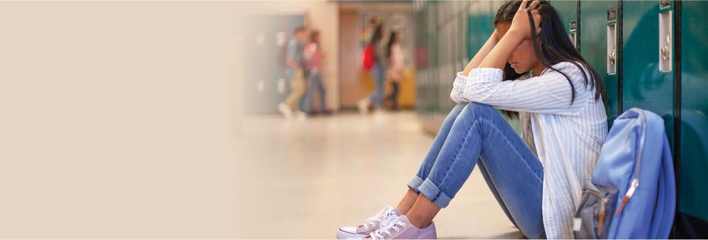Frustrated teenage female student sitting with head in hands. Side view of high school girl in illuminated corridor. She is against metallic lockers.