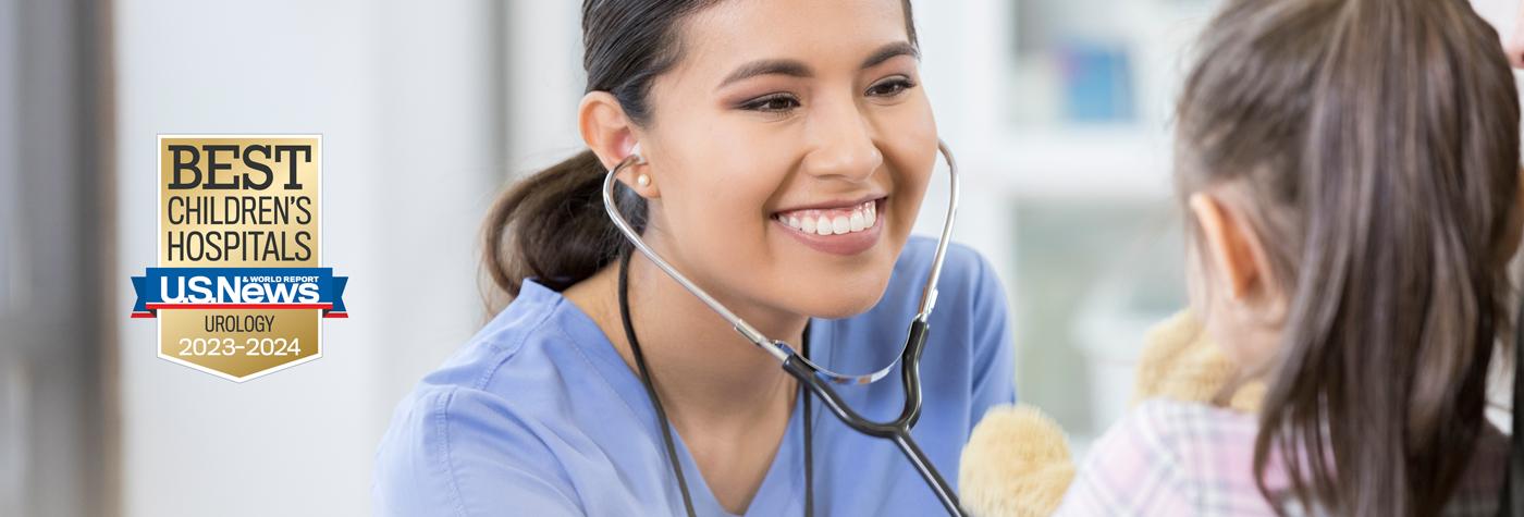 A female provider wearing a light blue scrub top and stethoscope smiles as she interacts with a young female patient. A badge on the photo reads U.S. News and World Report Best Children's Hospitals, Urology, 2023–2024.