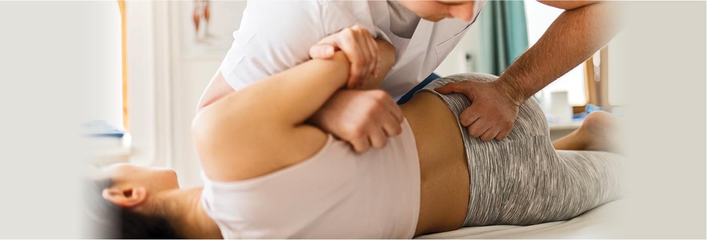 A physical therapist applies pressure to a female patient's lower back. 