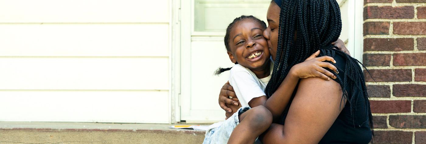 Mom hugs her young affectionate son on the outdoor stoop of a house