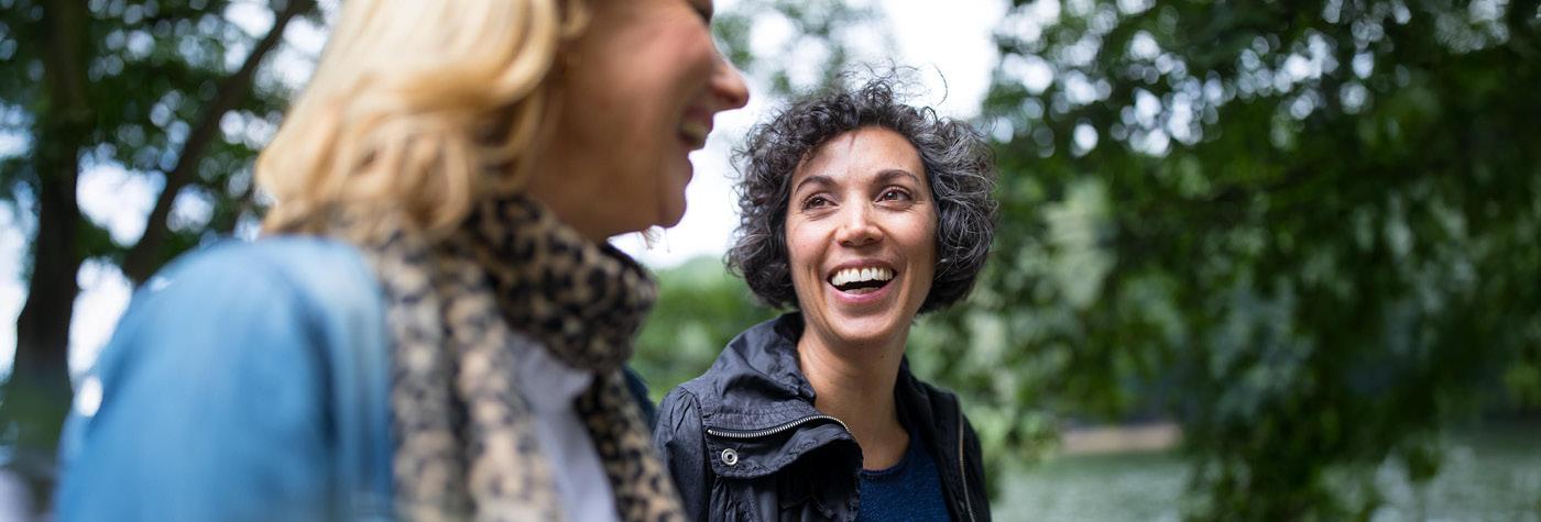 Two women smile as they walk side by side outdoors.