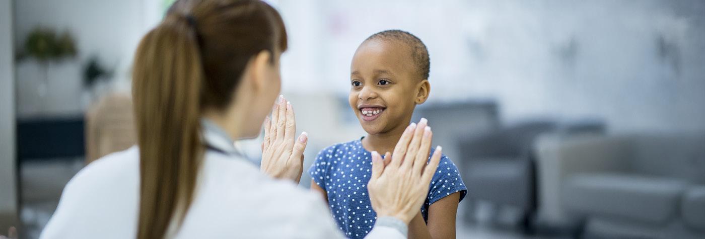 A doctor plays a clapping game with a young child, who we see smiling.